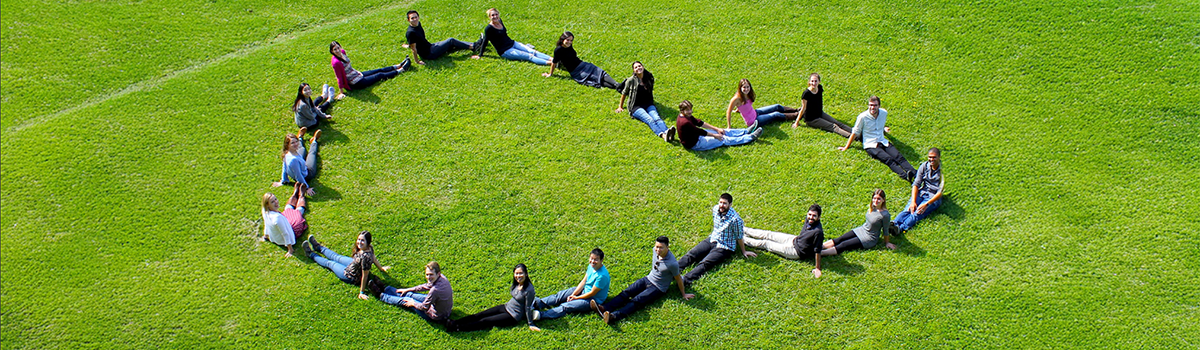 Image of students sitting together on grass representing community. PC: Ross Pederson